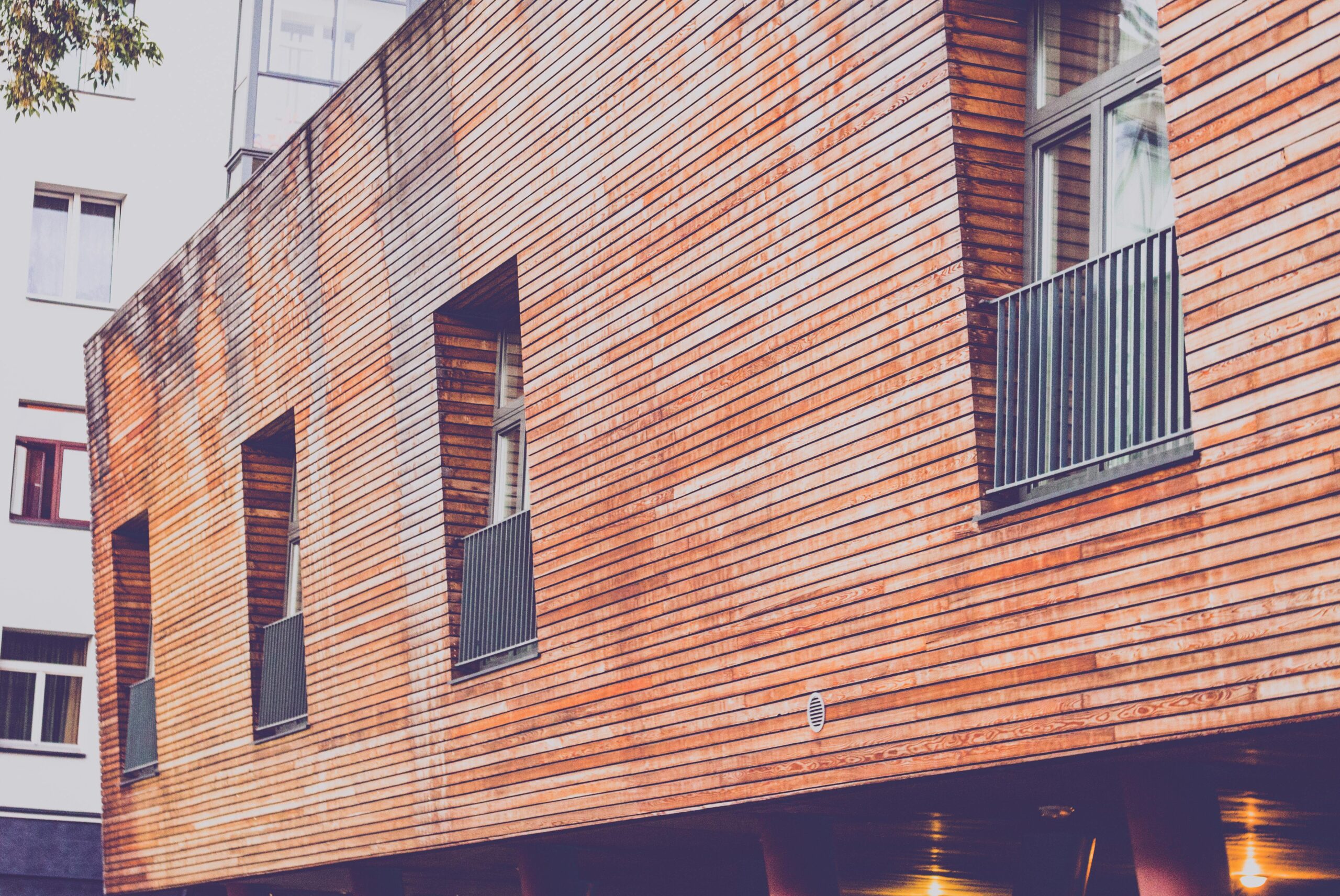 Contemporary wooden facade of a residential building with windows and railings, showcasing urban architecture.