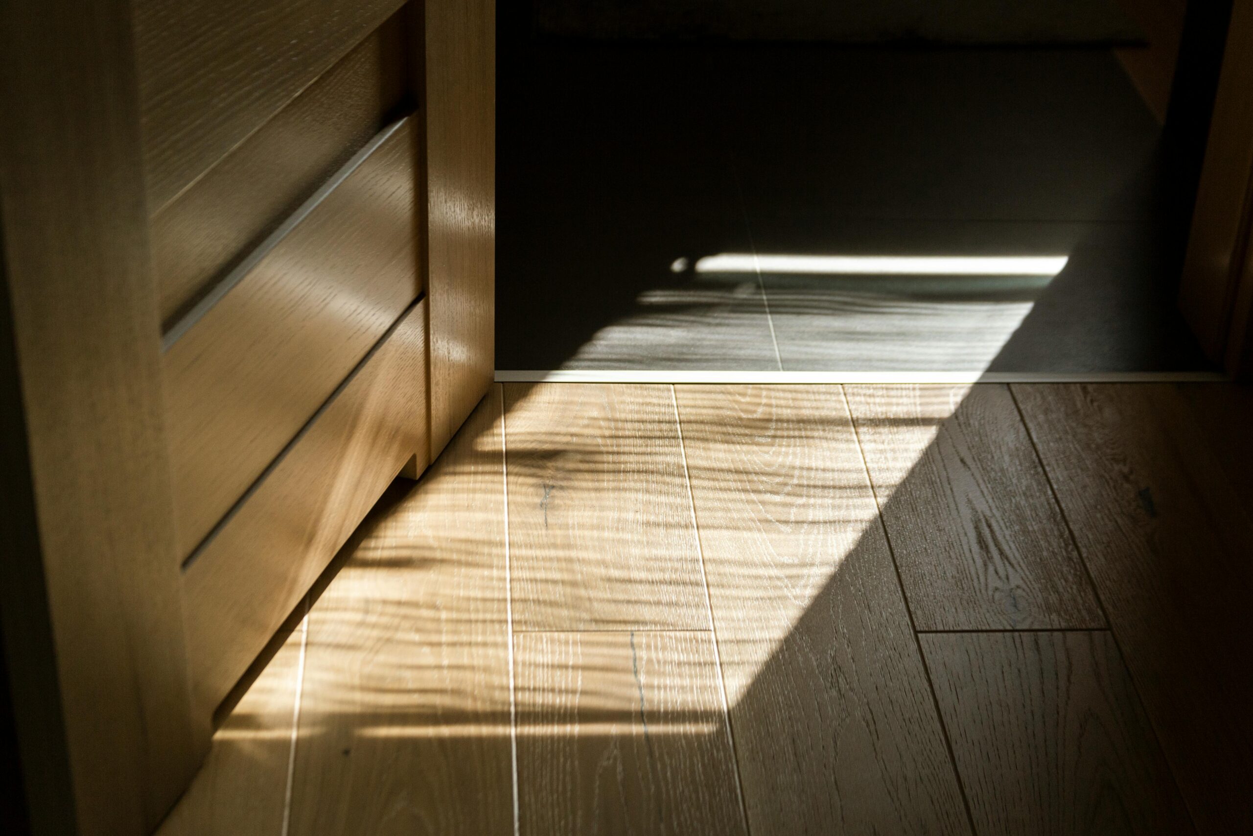 Sunlit shadows create patterns on a wooden parquet floor indoors.